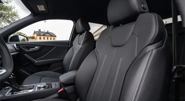 Interni Audi Q2: sedili in pelle nera con cuciture a contrasto, cambio automatico e un edificio storico sullo sfondo.