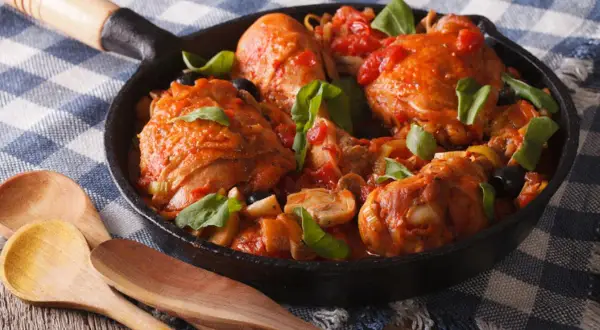 Pezzi di pollo succulenti in umido con pomodoro, olive e funghi, un delizioso coniglio alla cacciatora servito in padella.
