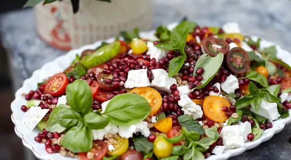 En färgglad coban salata med granatäpple, tomat, gurka, fetaost och basilika på ett vitt fat.