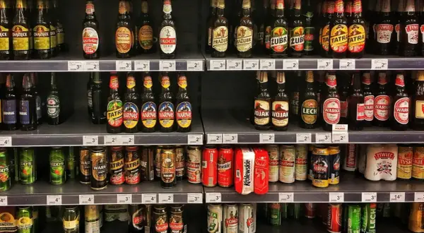 Półki sklepowe uginają się pod ciężarem piwa na półce. Butelki i puszki różnych marek tworzą kolorowy krajobraz.