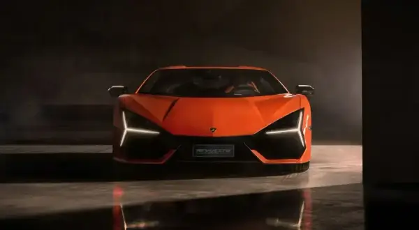 Pomarańczowy Lamborghini Revuelto z ostrymi światłami LED, odbijający się w mokrej podłodze.