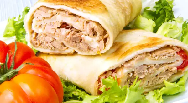 Dos rollos de wrap de atún, rellenos de atún desmenuzado y queso, servidos con lechuga fresca y tomates.