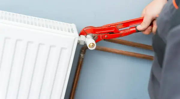 Mano con pinza rossa che lavora sulla valvola di un termosifone bianco, mostrando come smontare un termosifone.
