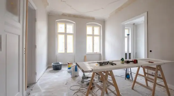 Mieszkanie na sprzedaż do remontu. Wnętrze w trakcie prac, widoczne materiały budowlane, drzwi na kozłach, okna i drzwi z żółtą taśmą.