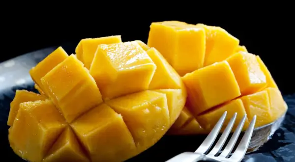 Soczyste, pokrojone w kostkę mango, jak na zdjęciu, budzi pozytywne african mango opinie. Widoczny widelec sugeruje gotowość do degustacji.