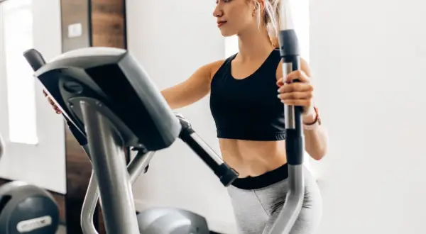 Junge Frau trainiert auf Crosstrainer, um ihren Kalorienverbrauch zu steigern.