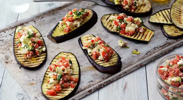 Grilla aubergine halvor toppade med en fräsch blandning av tomat, fetaost och örter. Perfekt som förrätt eller tillbehör.