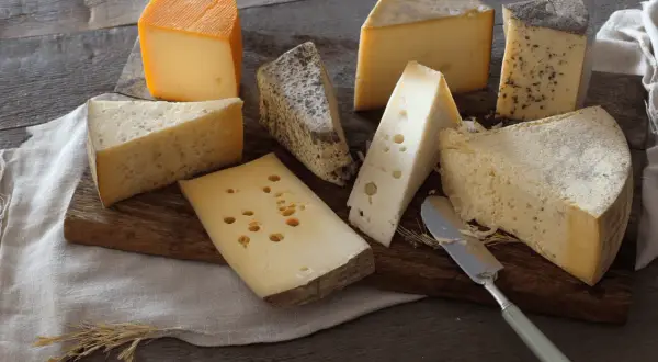 Assortiment de fromages, dont un beau morceau de comté pâte cuite, sur une planche en bois.