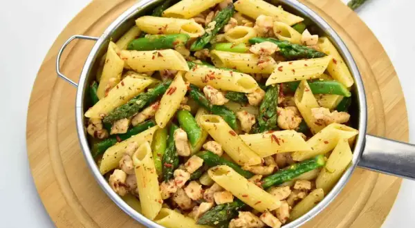 Penne z kurczakiem i szparagami, posypane papryką. Pyszne danie, które zachwyci każdego.