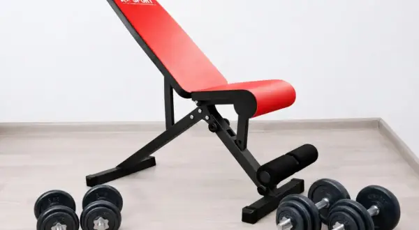 Rote Hantelbank mit schwarzem Rahmen und Hanteln auf dem Boden. Perfekt für dein Home-Gym, die beste Hantelbank für dein Training.