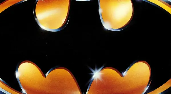 Logo Batmana z 1989 roku na tle gradientu pomarańczowo-żółtego.