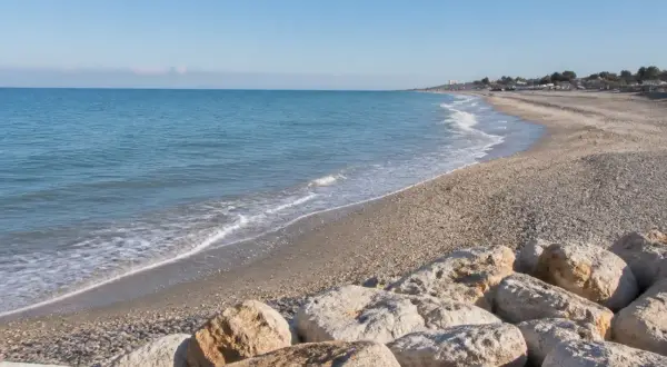 Spiaggia di Porto Sant'Elpidio Mare con rocce in primo piano e mare calmo sotto un cielo azzurro.