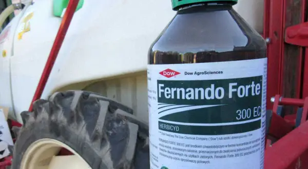 Butelka herbicydu Fernando Forte 300 EC na tle traktora.