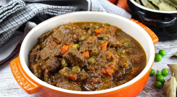 Ternera a la jardinera en un cuenco naranja, con trozos de carne tierna, guisantes y zanahoria en una rica salsa.
