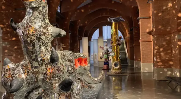 Sculptures de Niki de Saint Phalle, dont un dragon miroitant, dans un musée aux arches de briques.