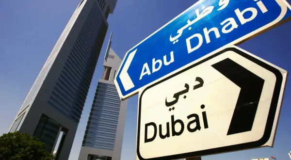 Znaki drogowe wskazują kierunek do Abu Zabi i Dubaju, na tle nowoczesnych wieżowców.