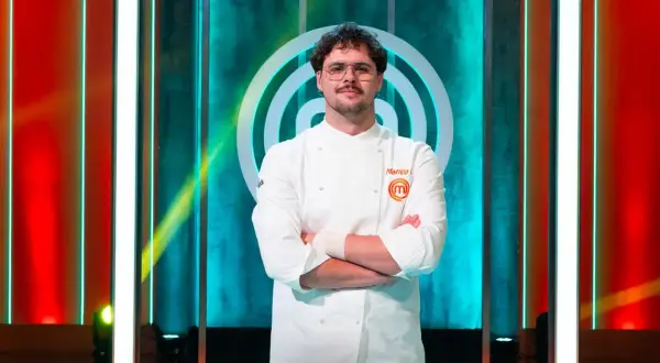 Matteo, vincitore MasterChef 15, posa con la sua divisa da chef, braccia conserte, sullo sfondo del logo del programma.