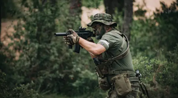 Hombre con camuflaje y pintura facial, listo para jugar airsoft que es un deporte de simulación de combate.
