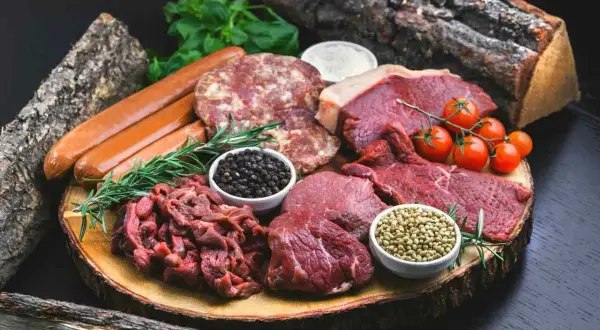 Mięsne bogactwo dla diety carnivore: steki, kiełbaski, mielone, pomidorki i przyprawy na drewnianej desce.