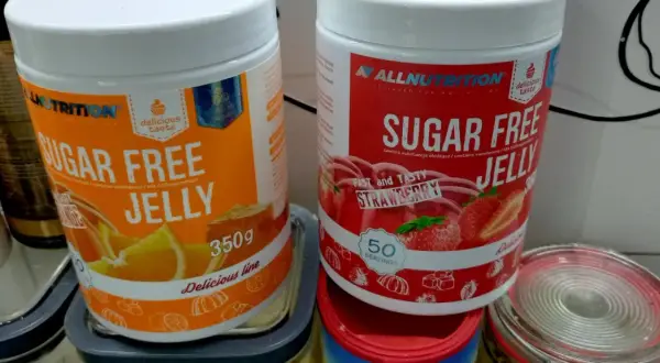 Dwie puszki galaretki bez cukru: pomarańczowa i truskawkowa. Zastanawiasz się, ile kalorii ma galaretka truskawkowa? Te produkty są niskokaloryczne.