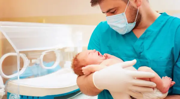Lekarz w maseczce i rękawiczkach trzyma noworodka, troskliwa neonatologia.