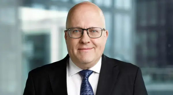 Mikael Staffas, en man med glasögon och kostym, ler mot kameran.