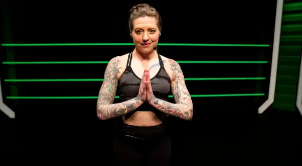 A tattooed woman in athletic wear holds her hands in prayer pose, ready for yoga for boxers.