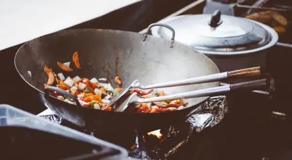 Wok med grönsaker som steks, med olika peppar sorter som ger smak. En gryta står i bakgrunden.