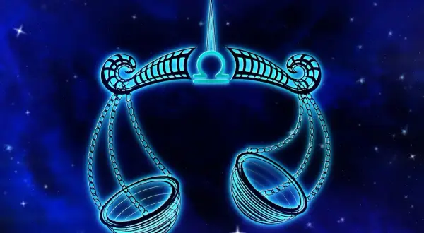Błękitna waga symbol zodiaku, jakby zrobiona z kamieni szlachetnych, unosi się na tle nocnego nieba pełnego gwiazd.