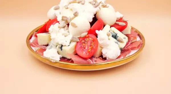 Sałatka z szynką parmeńską, serami, pomidorkami i słonecznikiem na złotym talerzu.