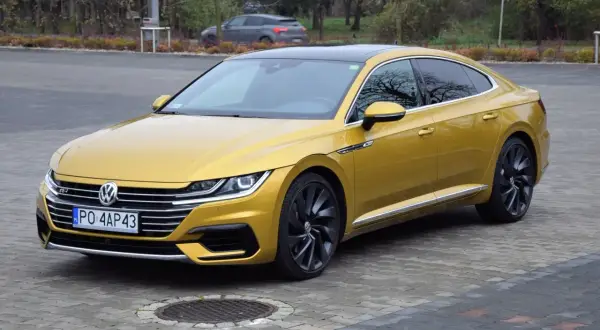 Złoty Volkswagen Arteon R z czarnym dachem i felgami, zaparkowany na bruku.