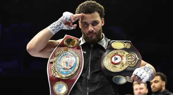 A boxer, champion of the super flyweight weight class, salutes with his championship belts.