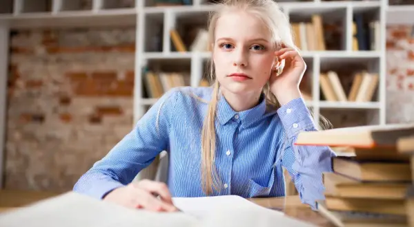 Młoda kobieta z blond włosami siedzi przy biurku, przed nią otwarte księgi. Przygotowuje wniosek o zwolnienie z kosztów sądowych.