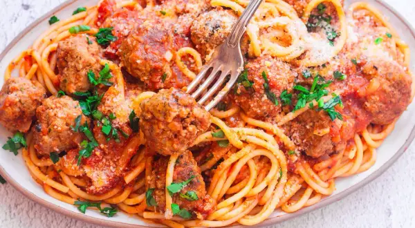 Pyszny makaron spaghetti z dziurką, polany sosem pomidorowym i posypany parmezanem, z soczystymi klopsikami.