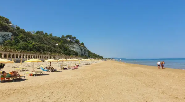 Spiaggia di ponente Rodi Garganico: sabbia dorata, ombrelloni gialli e un mare azzurro sotto un cielo limpido.