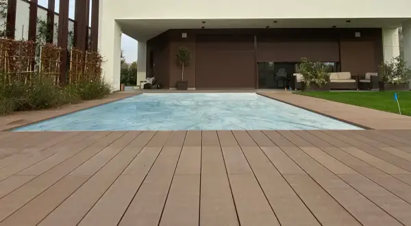 Ponte in legno effetto grana, ideale per esterni, circonda una piscina coperta. I requisiti dei pavimenti per esterni sono soddisfatti da questo materiale resistente e bello.