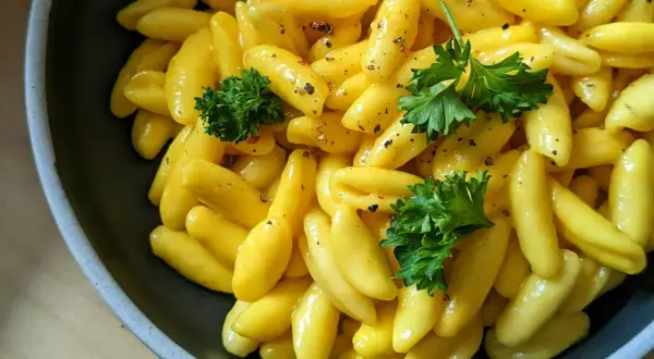 Żółty makaron gnocchi w sosie, udekorowany natką pietruszki i pieprzem, w ciemnej misce.