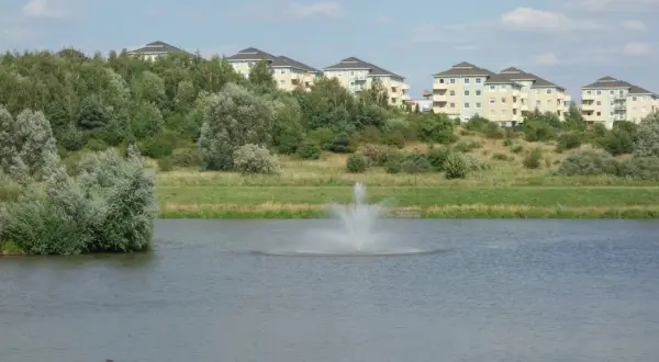 Widok na jezioro z fontanną i nowoczesne budynki mieszkalne na wzgórzu w Gdańsku Zakoniczyn.