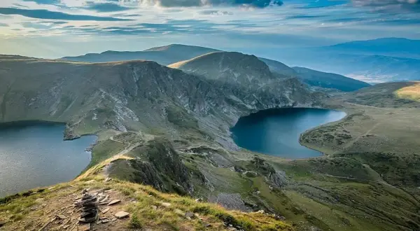 Vue panoramique d'un trek en Bulgarie. Des lacs glaciaires d'un bleu profond bordent des montagnes verdoyantes sous un ciel nuageux.