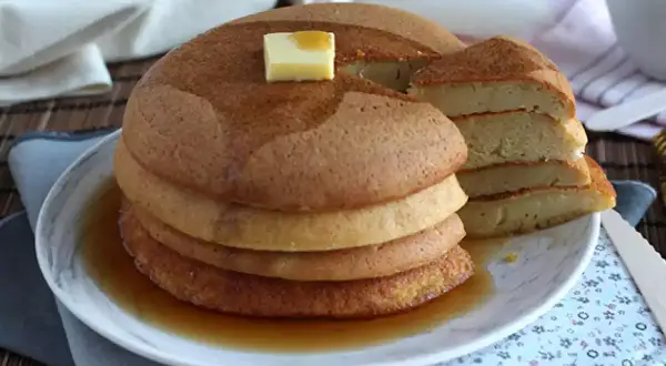 En hög med fluffiga japanska pannkakor, toppad med smör och sirap, serveras på en tallrik.