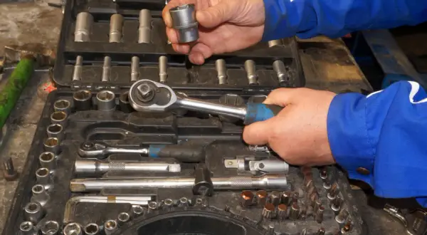 Wybieranie odpowiednich rozmiarów grzechotek z walizki narzędziowej. Ręce mechanika w niebieskim kombinezonie trzymają klucz i nasadkę.