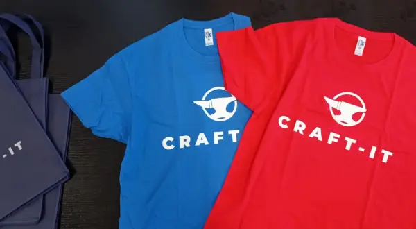 Niebieska i czerwona koszulka z logo "CRAFT-IT" i kowadłem. To przykład, jak sitodruk co to za technika, pozwala tworzyć trwałe nadruki na odzieży.