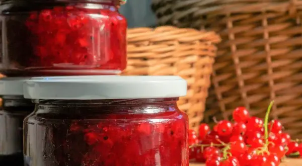 Słoiki z domowym dżemem z porzeczki czerwonej, obok świeże owoce. W tle plecione kosze.