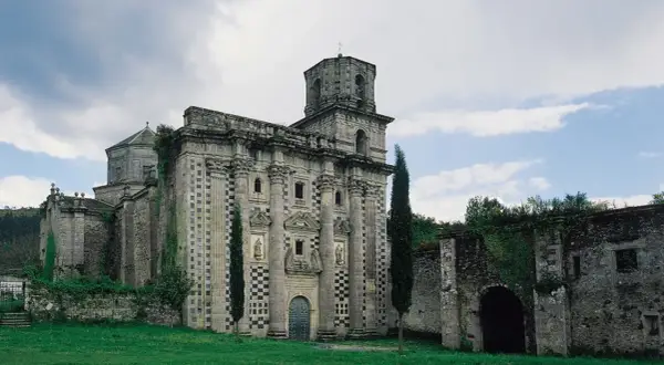 El imponente monasterio de Monfero, con su fachada de piedra y torre octogonal, se alza entre la vegetación, evocando historias de tiempos pasados.