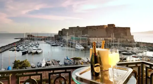 En balkong med champagne och glas, med en vy över hamnen och Castel Nuovo i Neapel.