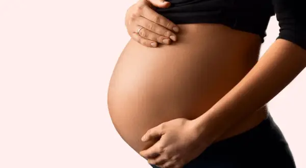 Schwanger und besorgt wegen eines Bandscheibenvorfalls? Die Hände einer Frau stützen sanft ihren runden Bauch.