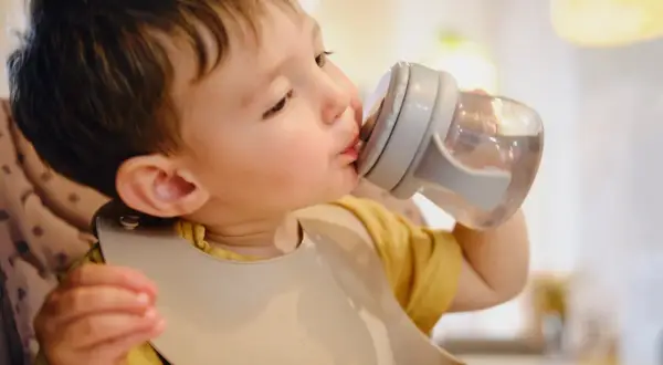 Un petit garçon boit de l'eau dans une tasse à bec, assurant son hydratation bébé.