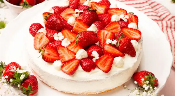 Eine köstliche Erdbeer-Sahne-Torte, üppig belegt mit frischen Erdbeerscheiben und Sahnetupfern, verziert mit kleinen weißen Blüten.