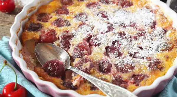 Pyszne clafoutis z wiśniami, posypane cukrem pudrem, czeka na łyżeczkę. Idealny deser na letnie popołudnie.