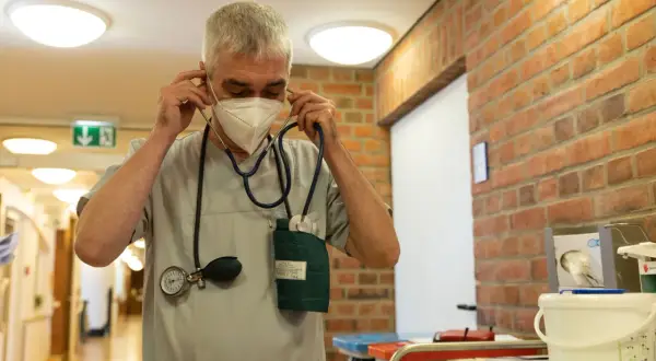 Mann mit Stethoskop und Maske im Flur, bereit für die Umschulung Gesundheits- und Krankenpfleger.